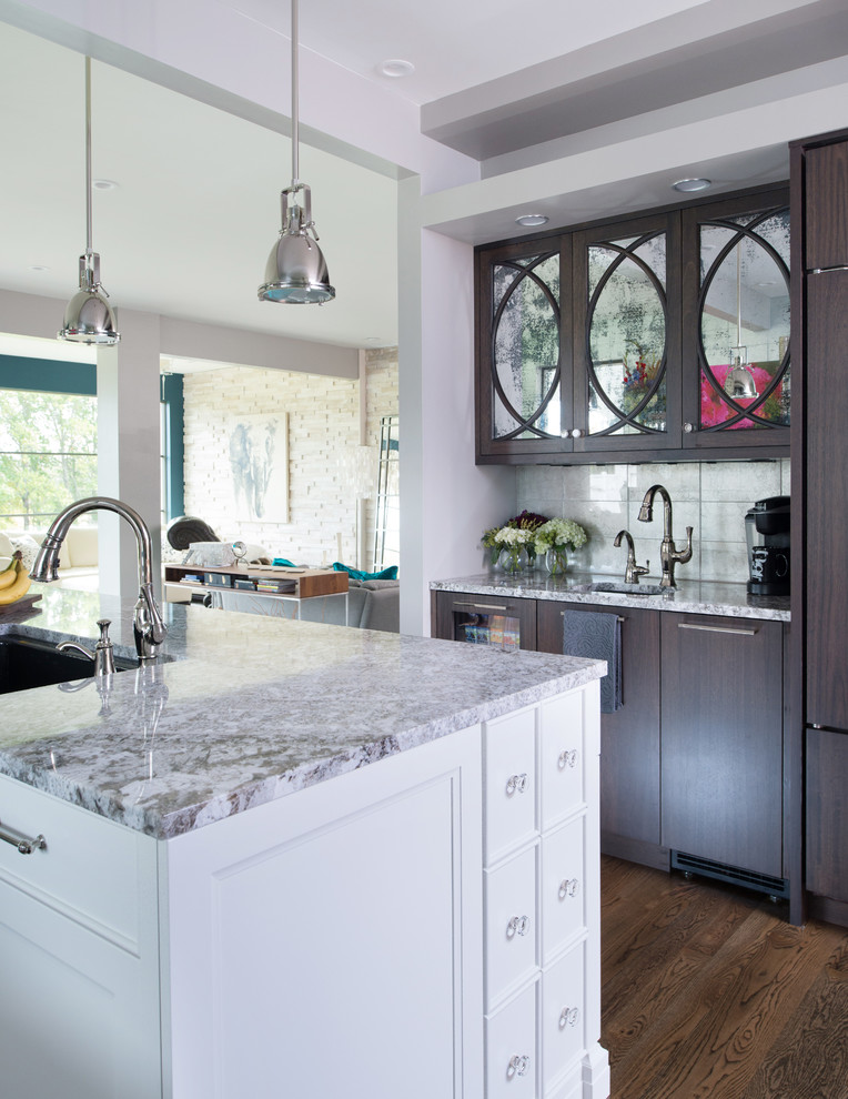 Inredning av ett klassiskt mellanstort kök, med en undermonterad diskho, luckor med infälld panel, vita skåp, granitbänkskiva, stänkskydd med metallisk yta, stänkskydd i glaskakel, rostfria vitvaror, mellanmörkt trägolv och en köksö