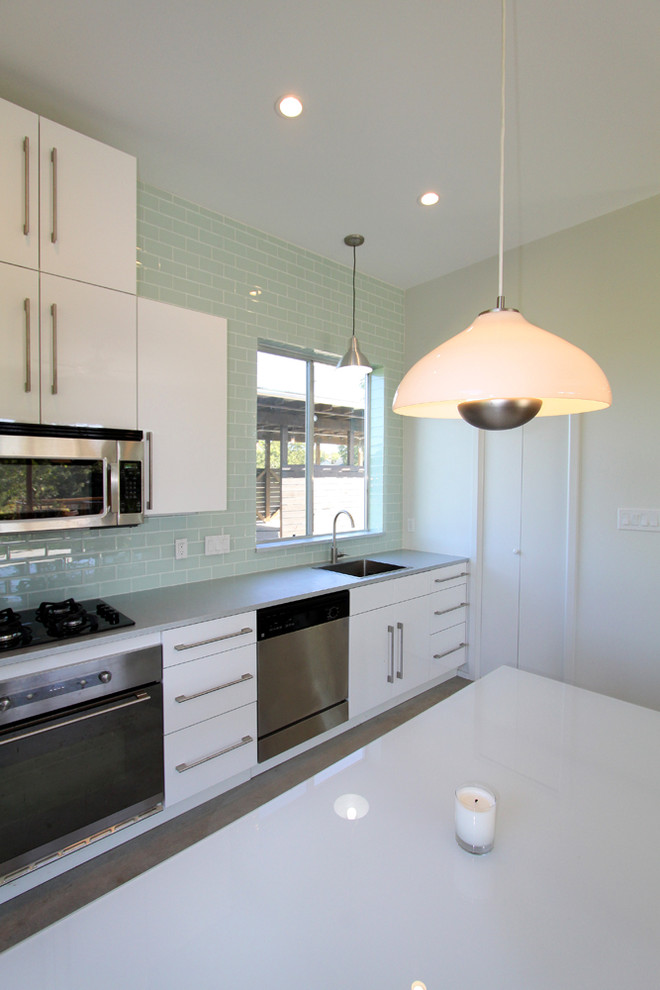 オースティンにある低価格のモダンスタイルのおしゃれなキッチン (シングルシンク、フラットパネル扉のキャビネット、白いキャビネット、緑のキッチンパネル、ガラスタイルのキッチンパネル、シルバーの調理設備) の写真