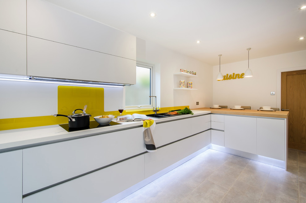 Moderne Küchenbar in L-Form mit Einbauwaschbecken, flächenbündigen Schrankfronten, weißen Schränken, Küchenrückwand in Gelb und Glasrückwand in Devon