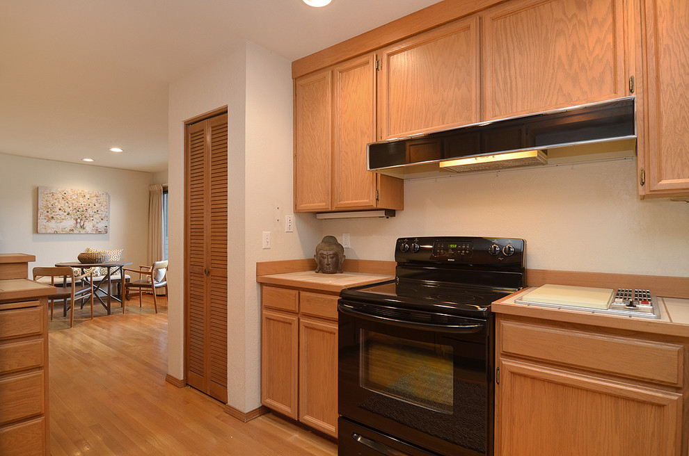 Mittelgroße Moderne Wohnküche in L-Form mit Schrankfronten mit vertiefter Füllung, Arbeitsplatte aus Fliesen, braunem Holzboden und Kücheninsel in Seattle