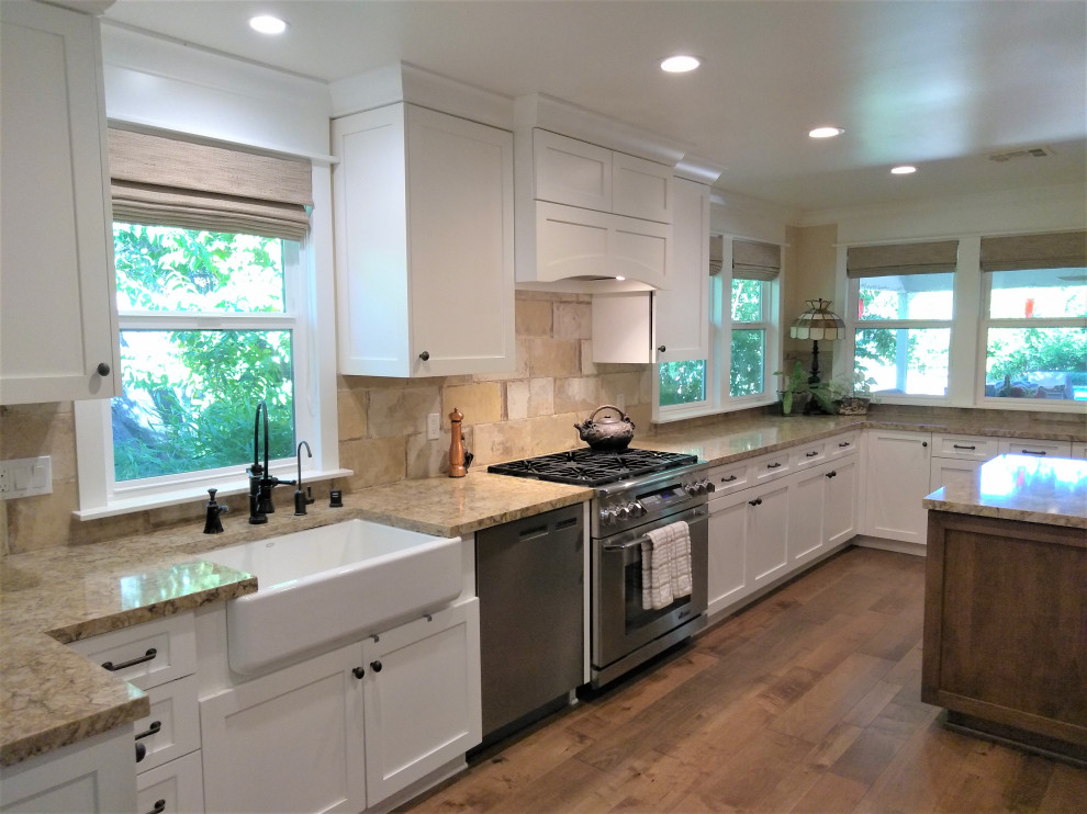 Large farmhouse open plan kitchen in Los Angeles with a belfast sink, shaker cabinets, white cabinets, engineered stone countertops, yellow splashback, stone tiled splashback, stainless steel appliances, medium hardwood flooring, an island, brown floors and yellow worktops.
