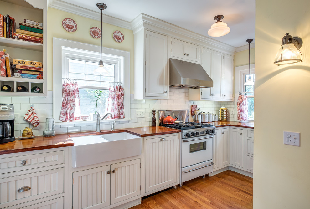 Inspiration for a small timeless u-shaped medium tone wood floor enclosed kitchen remodel in Other with a farmhouse sink, beaded inset cabinets, white cabinets, white backsplash, ceramic backsplash, wood countertops, white appliances and no island