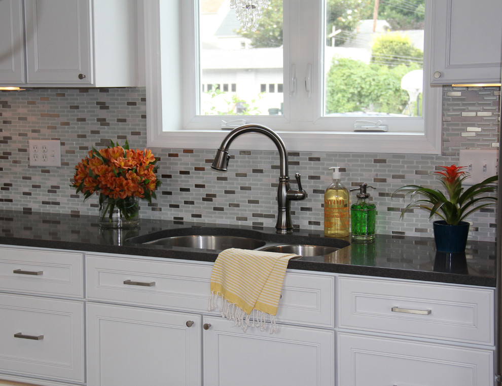 Bild på ett funkis kök, med luckor med infälld panel, vita skåp, bänkskiva i kvarts, blått stänkskydd, rostfria vitvaror, en dubbel diskho och mellanmörkt trägolv