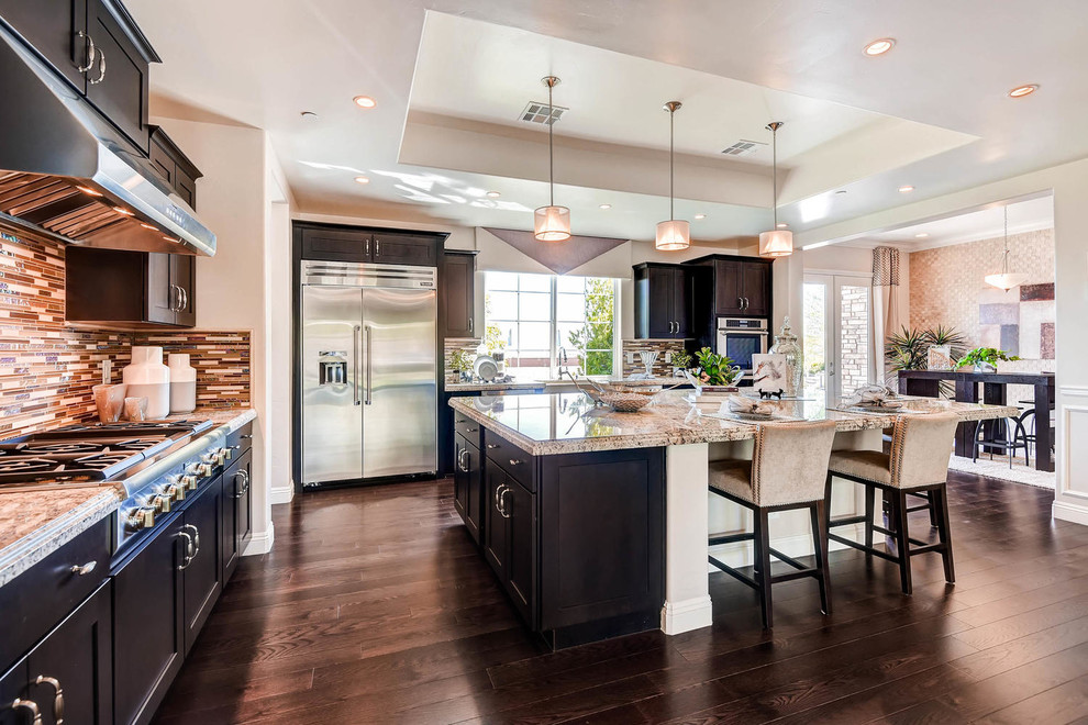 Large transitional l-shaped dark wood floor open concept kitchen photo in Las Vegas with an undermount sink, shaker cabinets, dark wood cabinets, granite countertops, metallic backsplash, glass tile backsplash, stainless steel appliances and an island