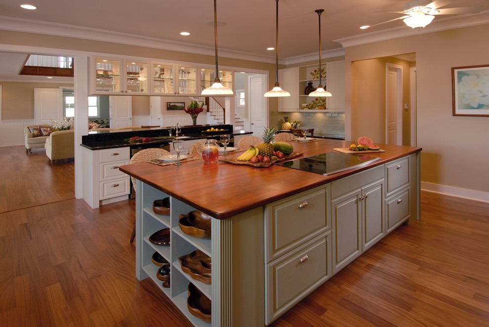 Example of an island style open concept kitchen design in Hawaii with raised-panel cabinets, wood countertops and green cabinets
