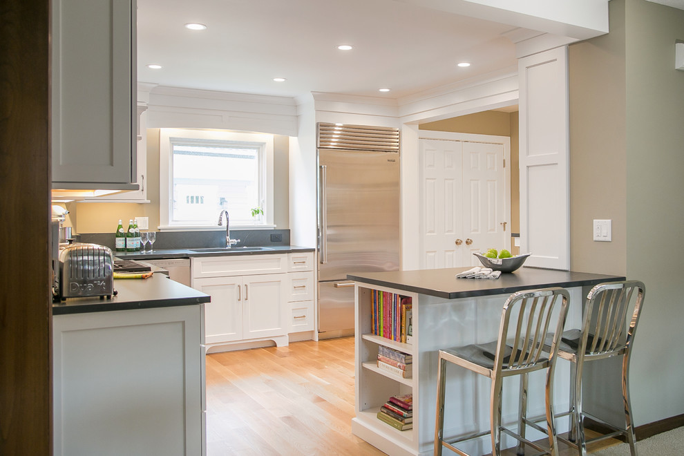Inspiration for a mid-sized farmhouse l-shaped light wood floor and beige floor enclosed kitchen remodel in Milwaukee with an undermount sink, white cabinets, stainless steel appliances, a peninsula, black countertops and shaker cabinets