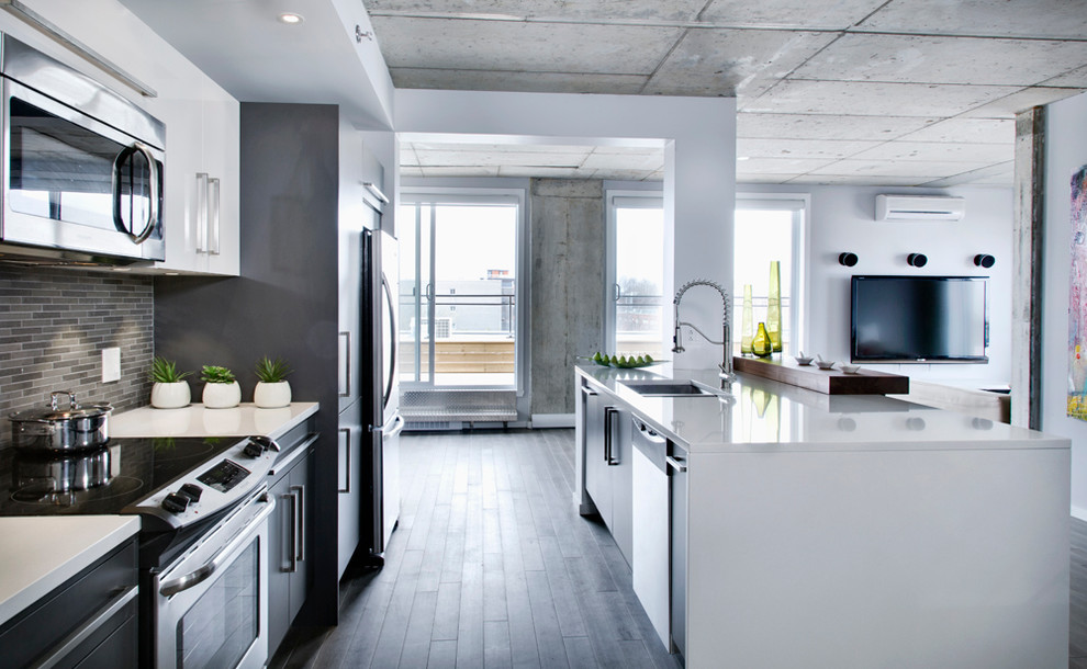 Example of a small minimalist single-wall dark wood floor open concept kitchen design in Montreal with an island, an undermount sink, flat-panel cabinets, white cabinets, quartz countertops, gray backsplash and stainless steel appliances