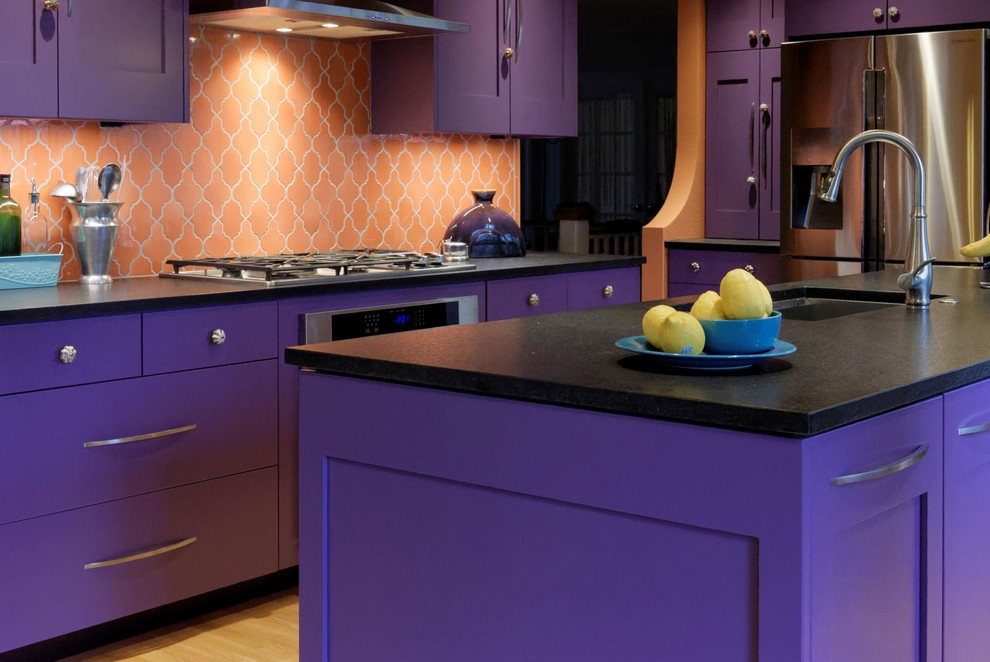 This is an example of a large mediterranean l-shaped enclosed kitchen in Portland with a submerged sink, shaker cabinets, purple cabinets, engineered stone countertops, orange splashback, ceramic splashback, stainless steel appliances, light hardwood flooring, an island, brown floors and black worktops.