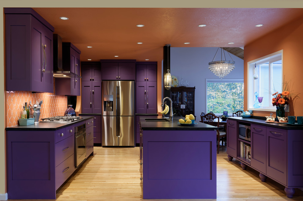 Inspiration for a large mediterranean l-shaped enclosed kitchen in Portland with a submerged sink, shaker cabinets, purple cabinets, engineered stone countertops, orange splashback, ceramic splashback, stainless steel appliances, light hardwood flooring, an island, brown floors and black worktops.