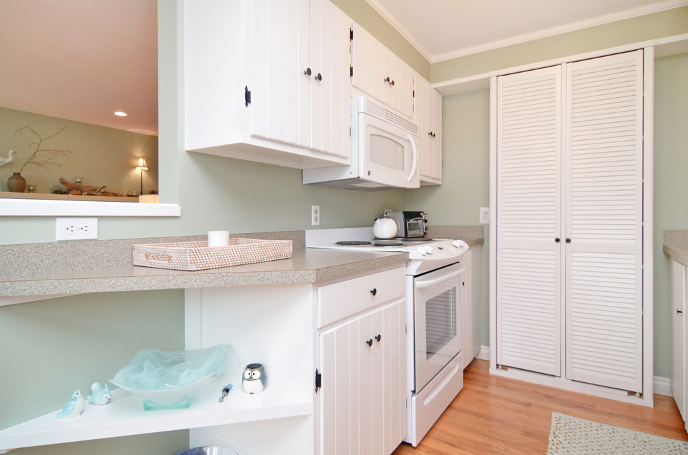 Exemple d'une petite cuisine américaine parallèle bord de mer avec un placard à porte affleurante, des portes de placard blanches, un plan de travail en stratifié, un électroménager blanc et parquet clair.