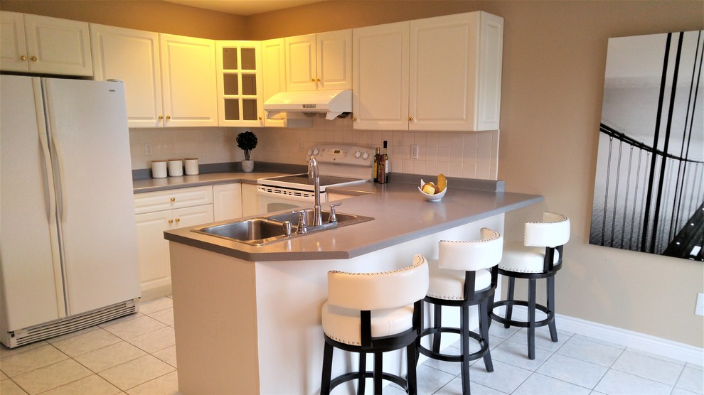 Exempel på ett litet klassiskt grå grått u-kök, med en dubbel diskho, luckor med upphöjd panel, vita skåp, laminatbänkskiva, vitt stänkskydd, stänkskydd i keramik, vita vitvaror, cementgolv, en halv köksö och vitt golv