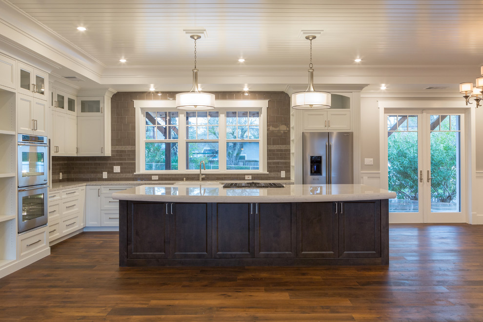Large classic l-shaped open plan kitchen in San Francisco with a belfast sink, recessed-panel cabinets, yellow cabinets, marble worktops, beige splashback, ceramic splashback, stainless steel appliances, dark hardwood flooring and an island.