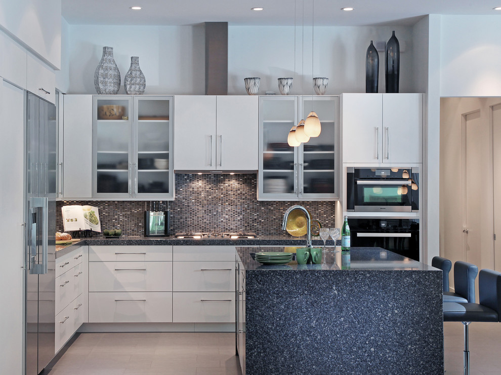 Example of a mid-sized trendy l-shaped porcelain tile and gray floor open concept kitchen design in Tampa with an undermount sink, flat-panel cabinets, white cabinets, gray backsplash, stone tile backsplash, stainless steel appliances, an island and quartz countertops