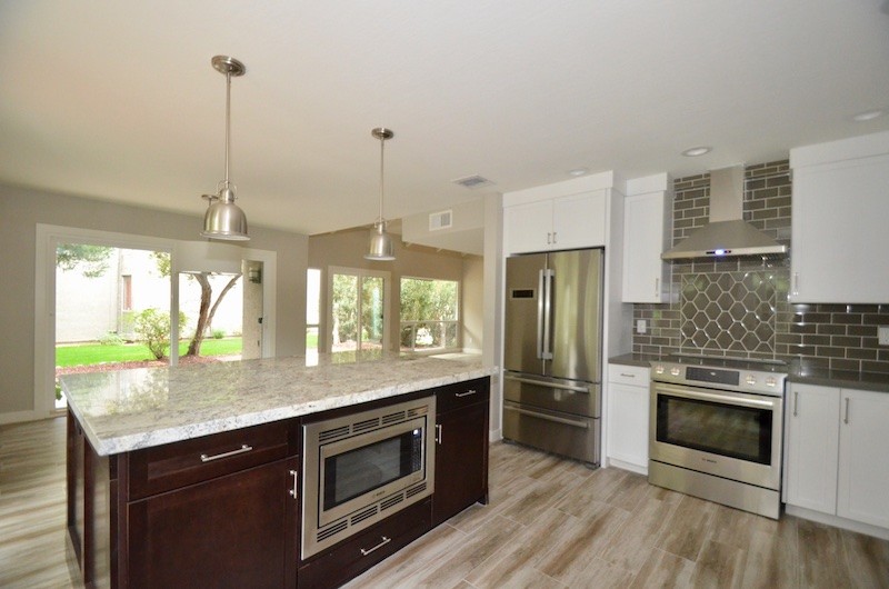 Example of a mid-sized mid-century modern l-shaped laminate floor and beige floor eat-in kitchen design in Phoenix with an undermount sink, shaker cabinets, granite countertops, beige backsplash, subway tile backsplash, stainless steel appliances and an island