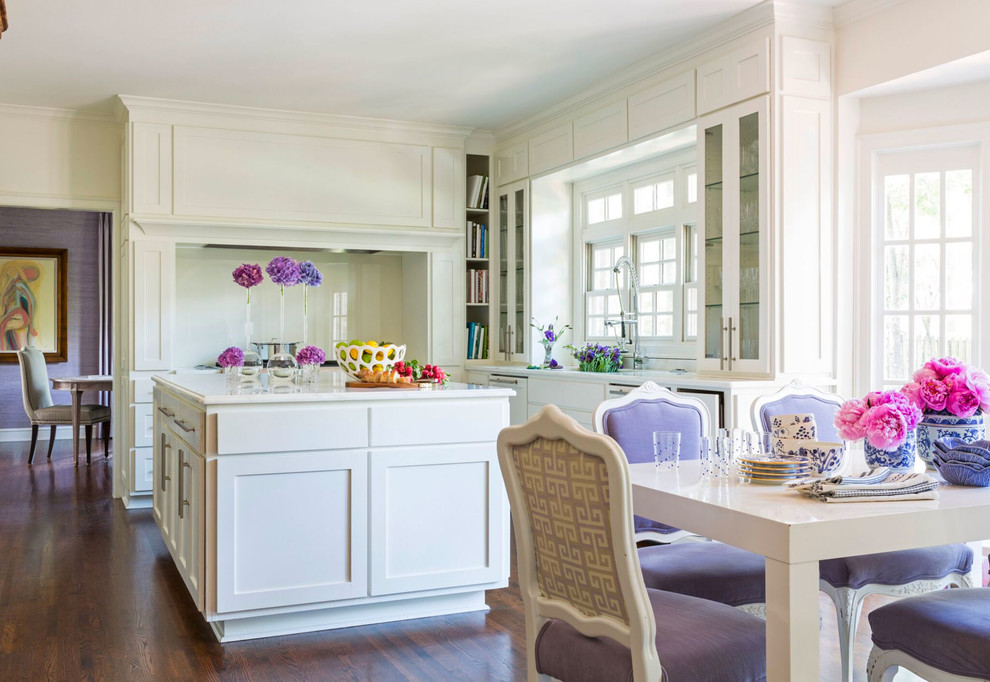 Klassisk inredning av ett stort kök och matrum, med luckor med glaspanel, vita skåp, marmorbänkskiva, fönster som stänkskydd, mellanmörkt trägolv och en köksö