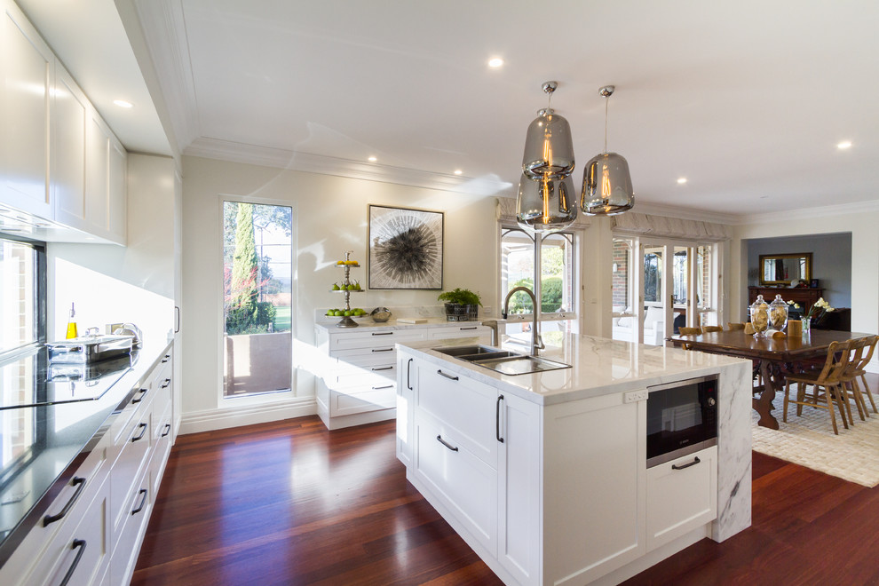 Photo of a large contemporary u-shaped kitchen/diner in Melbourne with a submerged sink, white cabinets, marble worktops, white splashback, window splashback, dark hardwood flooring, an island, brown floors, white worktops, recessed-panel cabinets and stainless steel appliances.