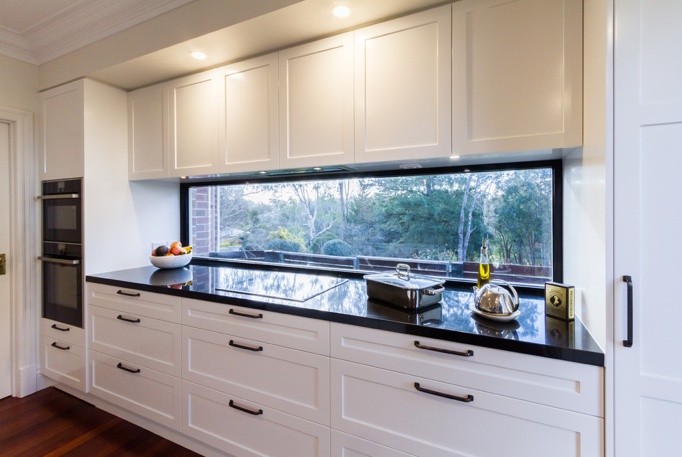 Example of a large trendy u-shaped dark wood floor and brown floor eat-in kitchen design in Melbourne with an undermount sink, shaker cabinets, white cabinets, marble countertops, white backsplash, window backsplash, black appliances, an island and white countertops