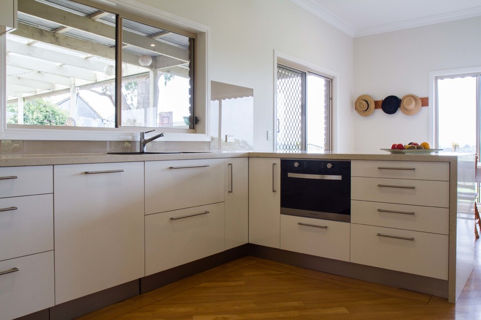 Immagine di una cucina design di medie dimensioni con ante lisce, ante bianche, top in quarzo composito, paraspruzzi beige, paraspruzzi con lastra di vetro e penisola