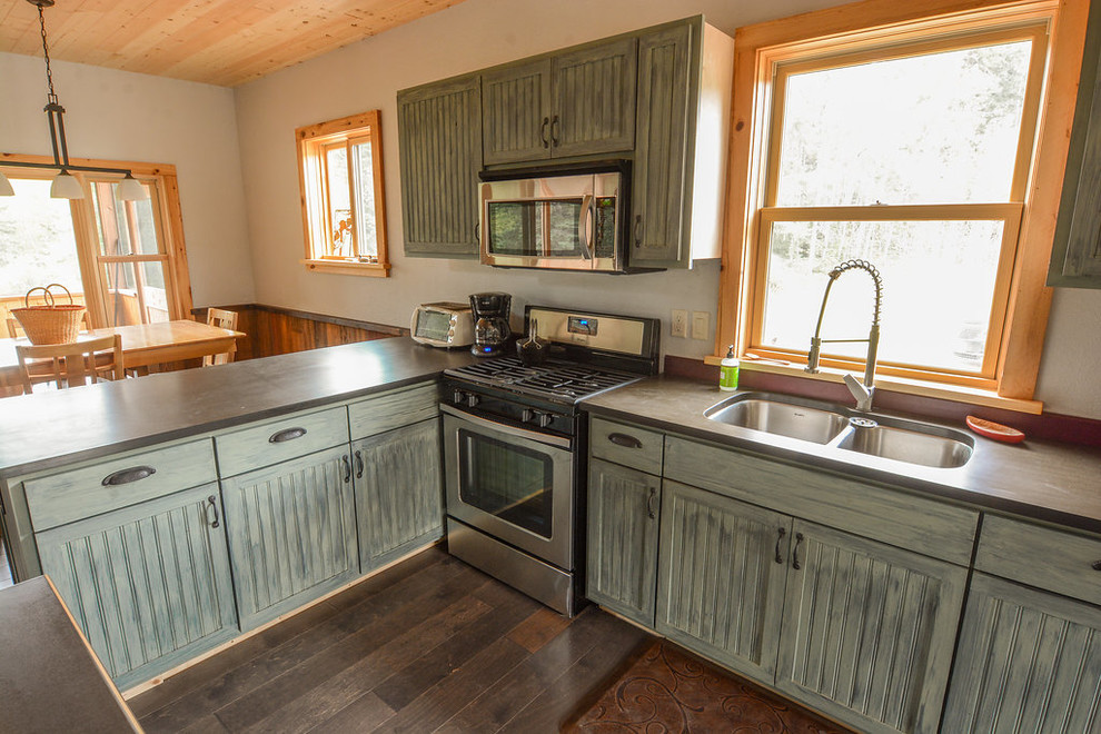 Inredning av ett rustikt mellanstort kök, med en dubbel diskho, luckor med profilerade fronter, skåp i slitet trä, laminatbänkskiva, rostfria vitvaror, mörkt trägolv och en köksö