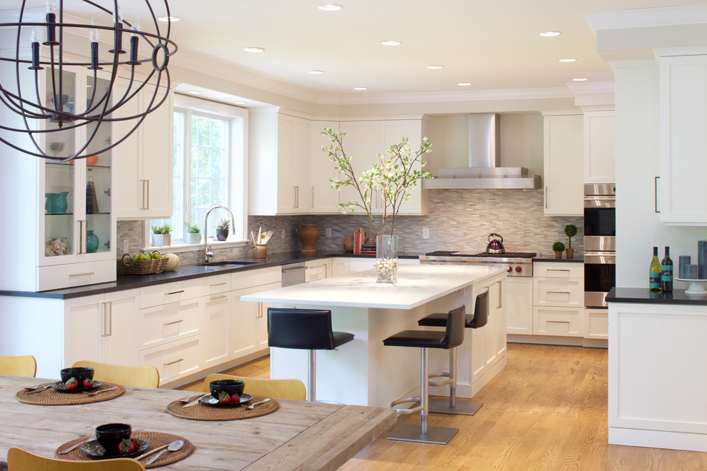 Eat-in kitchen - mid-sized contemporary l-shaped light wood floor eat-in kitchen idea in New York with an undermount sink, flat-panel cabinets, white cabinets, solid surface countertops, gray backsplash, glass tile backsplash, paneled appliances and an island