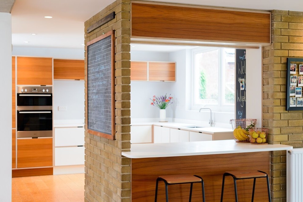 Exemple d'une cuisine rétro avec un évier encastré, un placard à porte plane, des portes de placard blanches, un sol en bois brun et une péninsule.