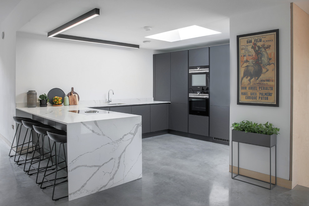 Photo of a medium sized contemporary u-shaped kitchen in Essex with flat-panel cabinets, grey cabinets, marble worktops, white splashback, marble splashback, integrated appliances, concrete flooring, a breakfast bar, grey floors, white worktops and a submerged sink.