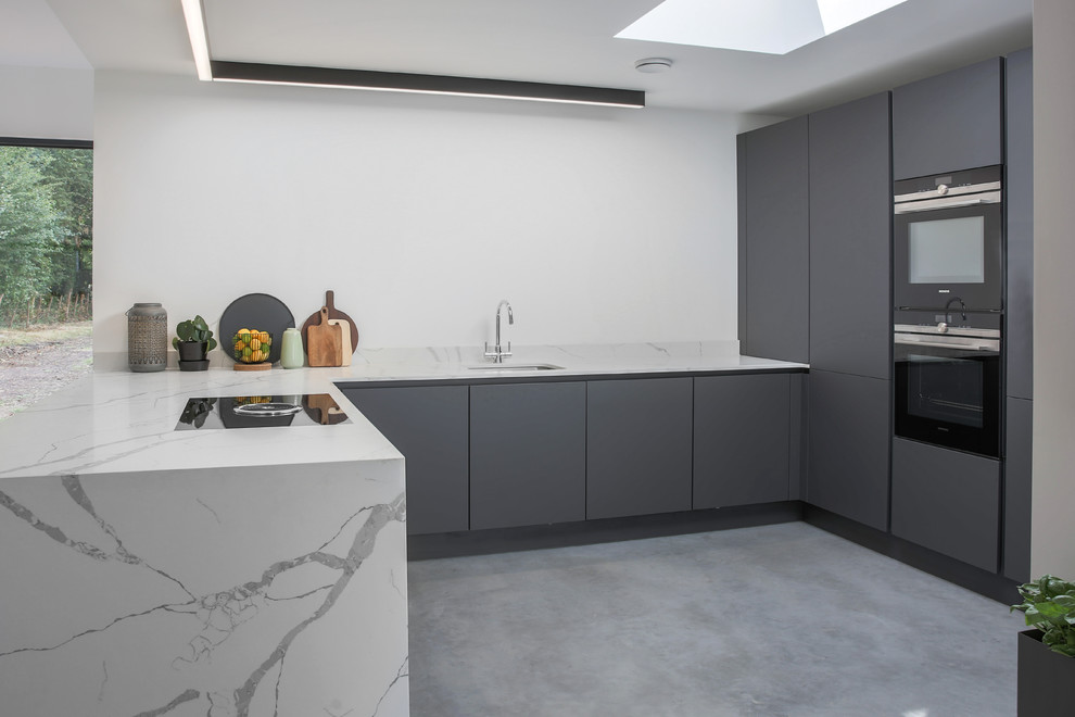 Inredning av ett modernt mellanstort vit vitt kök, med en integrerad diskho, släta luckor, grå skåp, marmorbänkskiva, vitt stänkskydd, stänkskydd i marmor, integrerade vitvaror, betonggolv, en halv köksö och grått golv