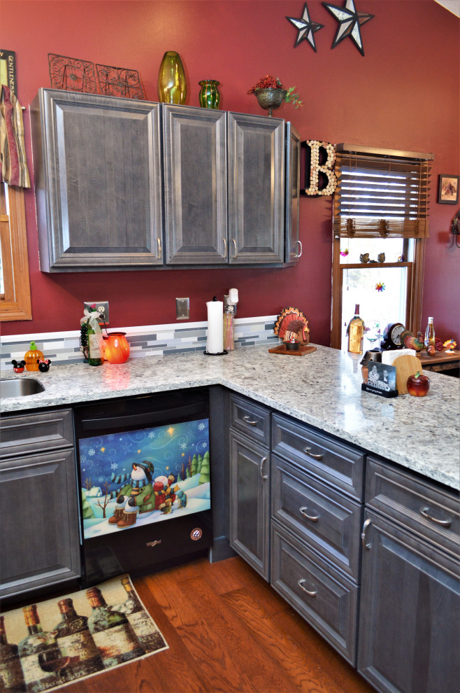 Klassisk inredning av ett mellanstort grå grått kök, med en undermonterad diskho, luckor med upphöjd panel, grå skåp, bänkskiva i kvartsit, flerfärgad stänkskydd, stänkskydd i stickkakel, svarta vitvaror, mellanmörkt trägolv, en halv köksö och brunt golv