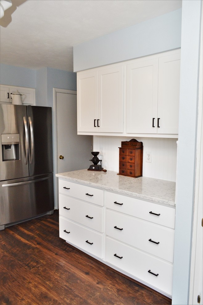 Lantlig inredning av ett mellanstort vit vitt kök, med en undermonterad diskho, skåp i shakerstil, vita skåp, bänkskiva i kvartsit, vitt stänkskydd, stänkskydd i trä, rostfria vitvaror och brunt golv