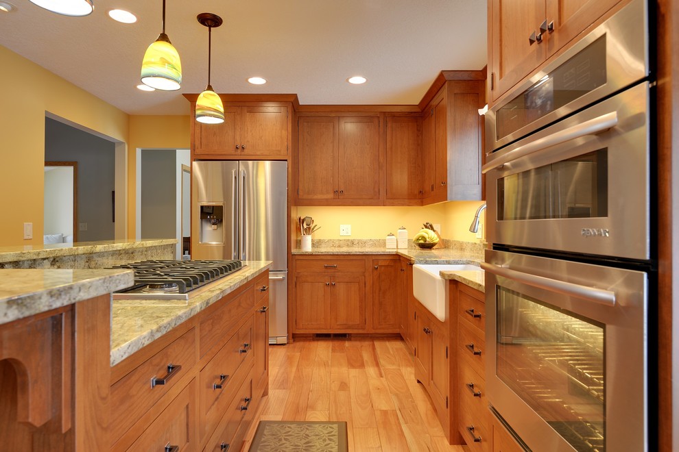 Mittelgroße Urige Küche mit Landhausspüle, Schrankfronten im Shaker-Stil, hellbraunen Holzschränken, Granit-Arbeitsplatte, Küchengeräten aus Edelstahl, braunem Holzboden und Kücheninsel in Minneapolis
