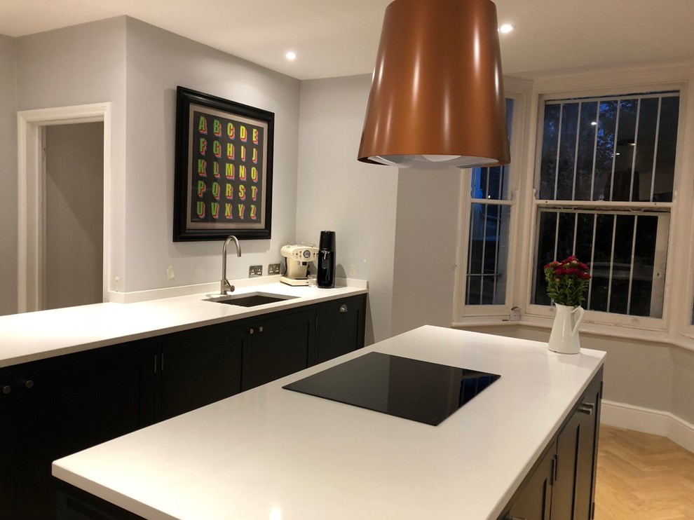 Medium sized classic open plan kitchen in London with an integrated sink, shaker cabinets, black cabinets, quartz worktops, integrated appliances, light hardwood flooring, an island, brown floors and white worktops.