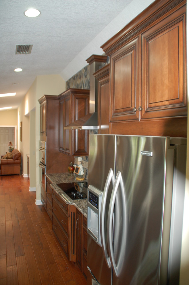Cette photo montre une petite cuisine américaine tendance avec un placard avec porte à panneau encastré, un plan de travail en granite, une crédence bleue, un électroménager en acier inoxydable et un sol en bois brun.