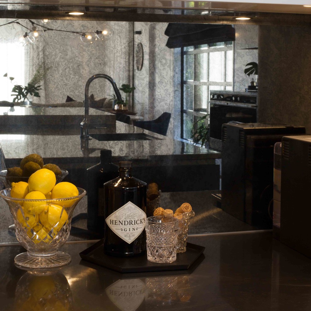 Modern inredning av ett grå grått kök, med vita skåp, granitbänkskiva, stänkskydd med metallisk yta, glaspanel som stänkskydd och mellanmörkt trägolv