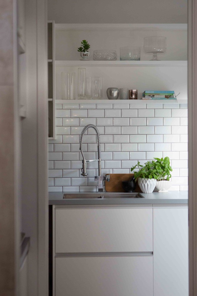 Ejemplo de cocinas en L moderna con despensa, suelo de madera en tonos medios, puertas de armario blancas, encimera de laminado, salpicadero blanco, salpicadero de azulejos de cemento y encimeras grises