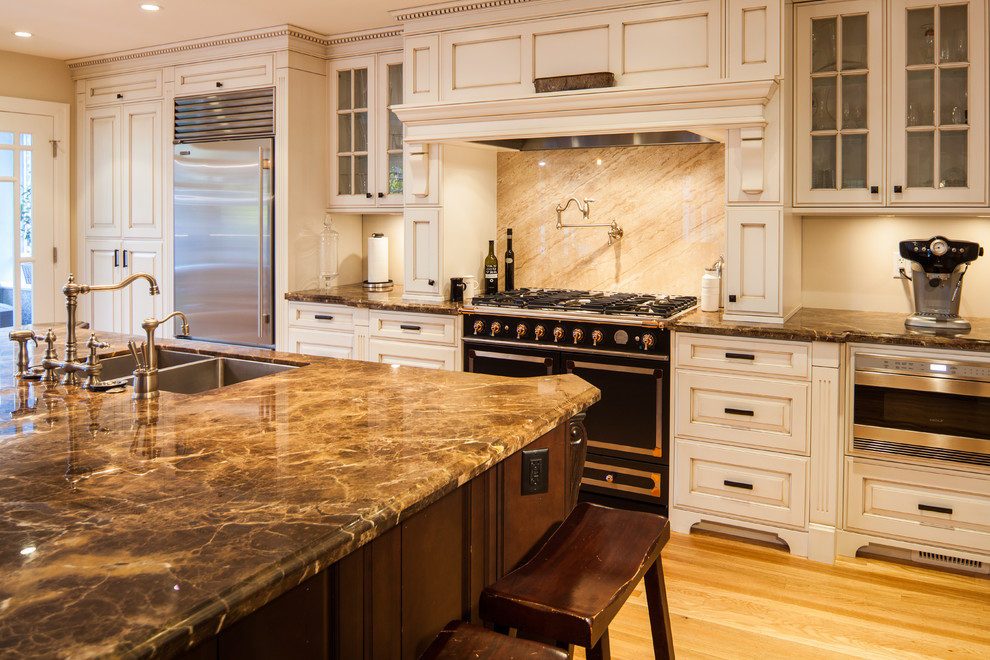 Klassisk inredning av ett mellanstort kök, med en undermonterad diskho, luckor med upphöjd panel, vita skåp, marmorbänkskiva, beige stänkskydd, stänkskydd i sten, rostfria vitvaror, ljust trägolv och en köksö