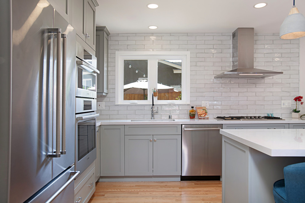 Kitchen - mid-sized transitional l-shaped medium tone wood floor kitchen idea in San Diego with an undermount sink, flat-panel cabinets, gray cabinets, quartz countertops, white backsplash, porcelain backsplash, stainless steel appliances, an island and white countertops