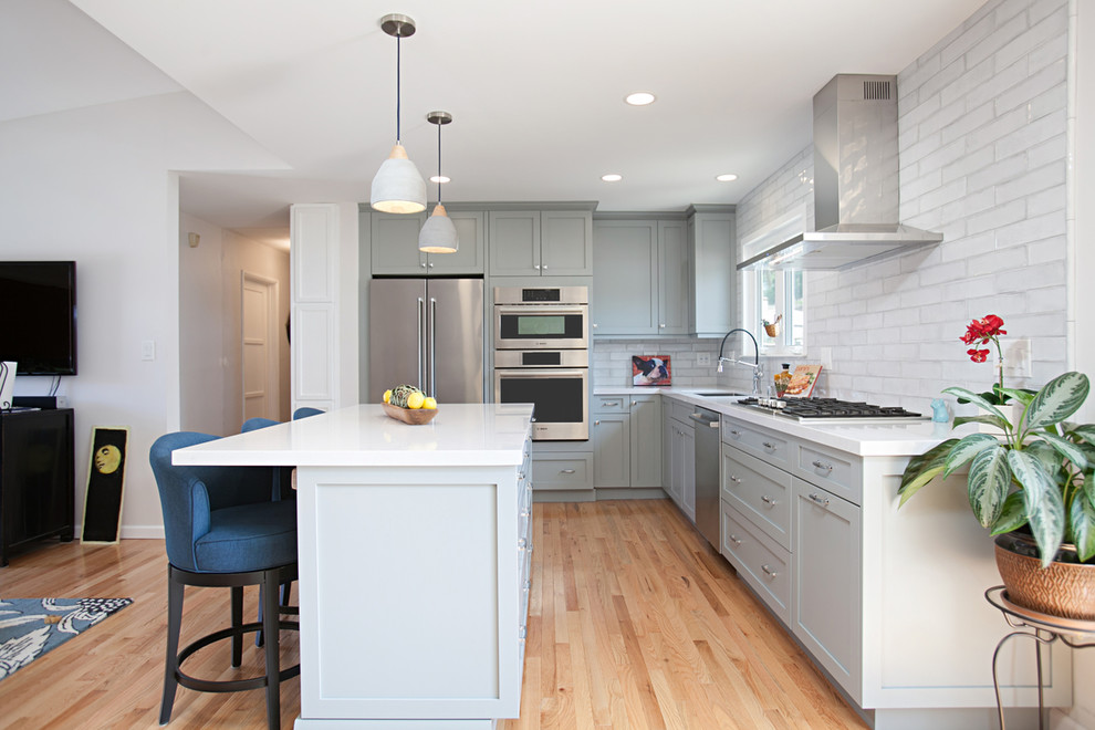 Inspiration for a mid-sized transitional l-shaped medium tone wood floor kitchen remodel in San Diego with an undermount sink, flat-panel cabinets, gray cabinets, quartz countertops, white backsplash, porcelain backsplash, stainless steel appliances, an island and white countertops