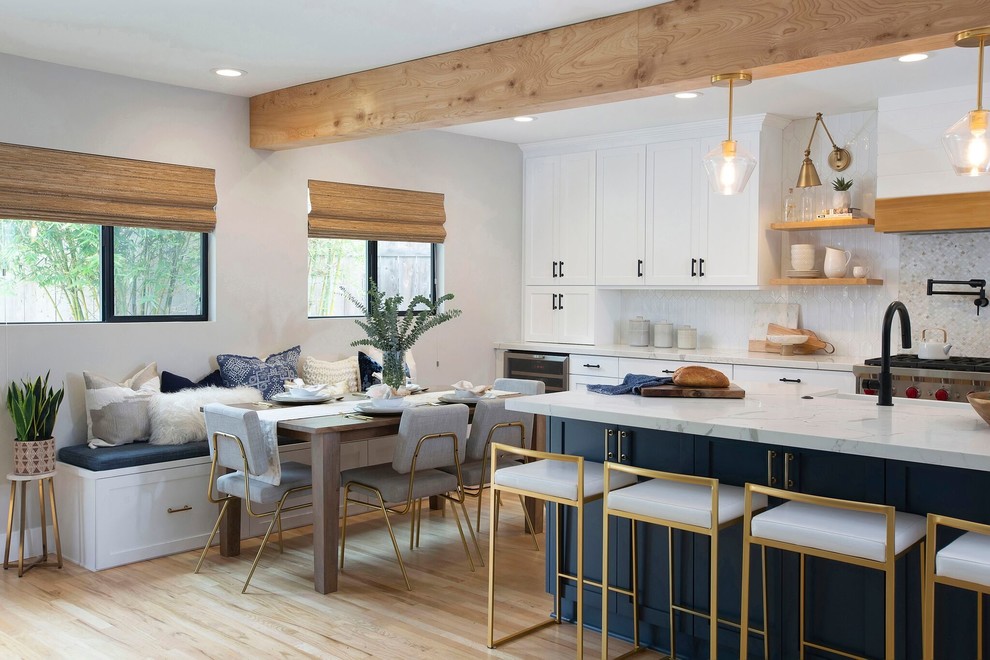 Mid-sized transitional single-wall light wood floor and beige floor open concept kitchen photo in Denver with a farmhouse sink, shaker cabinets, white cabinets, quartz countertops, white backsplash, ceramic backsplash, stainless steel appliances, an island and white countertops