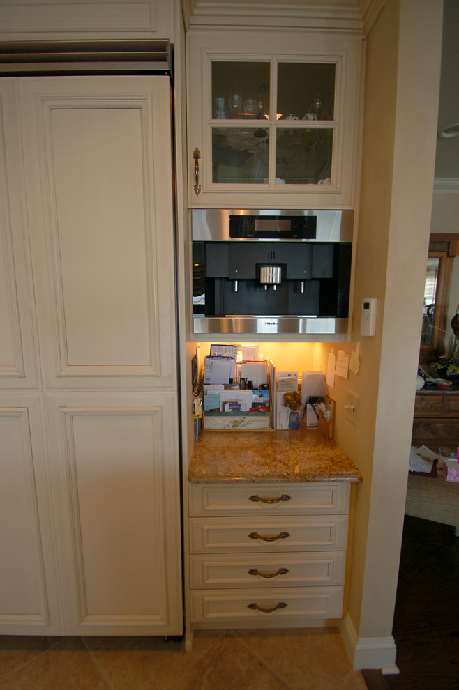 Klassisk inredning av ett stort kök, med en undermonterad diskho, luckor med infälld panel, vita skåp, granitbänkskiva, beige stänkskydd, integrerade vitvaror, kalkstensgolv och en köksö