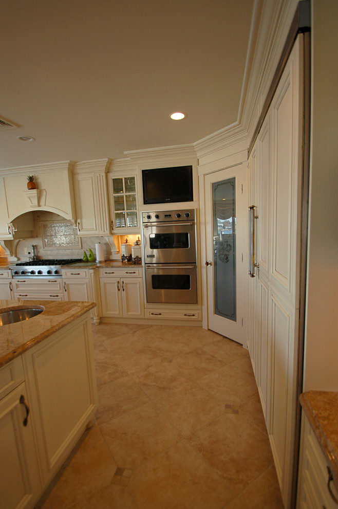 Exempel på ett stort klassiskt kök, med en undermonterad diskho, luckor med infälld panel, vita skåp, granitbänkskiva, beige stänkskydd, integrerade vitvaror, kalkstensgolv och en köksö