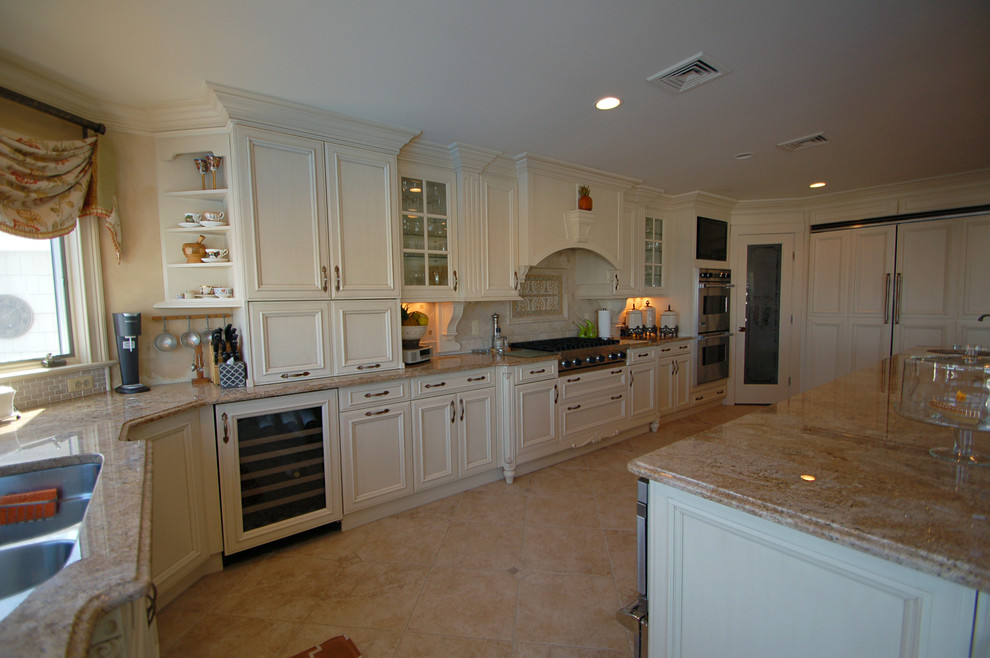Foto på ett stort vintage kök, med en undermonterad diskho, luckor med infälld panel, vita skåp, granitbänkskiva, beige stänkskydd, integrerade vitvaror, kalkstensgolv och en köksö