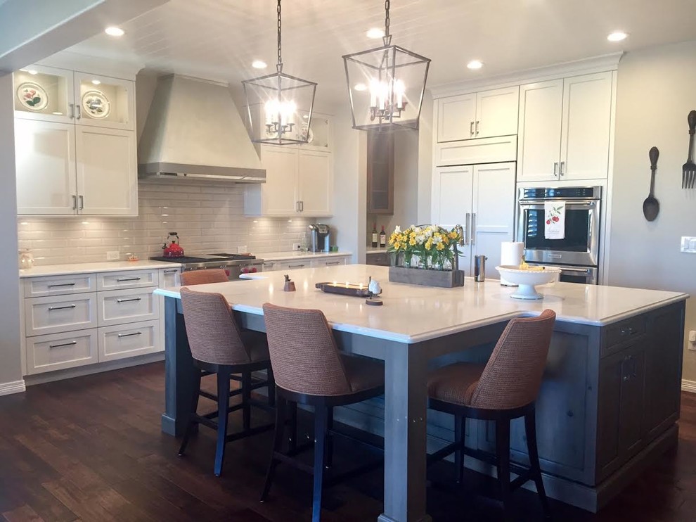 Large transitional single-wall medium tone wood floor and brown floor kitchen photo in Denver with shaker cabinets, white cabinets, white backsplash, subway tile backsplash, stainless steel appliances and an island