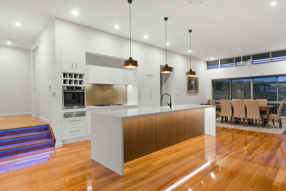 Contemporary kitchen/diner in Other with a single-bowl sink, flat-panel cabinets, white cabinets, brown splashback, glass sheet splashback, stainless steel appliances, medium hardwood flooring, an island and white worktops.