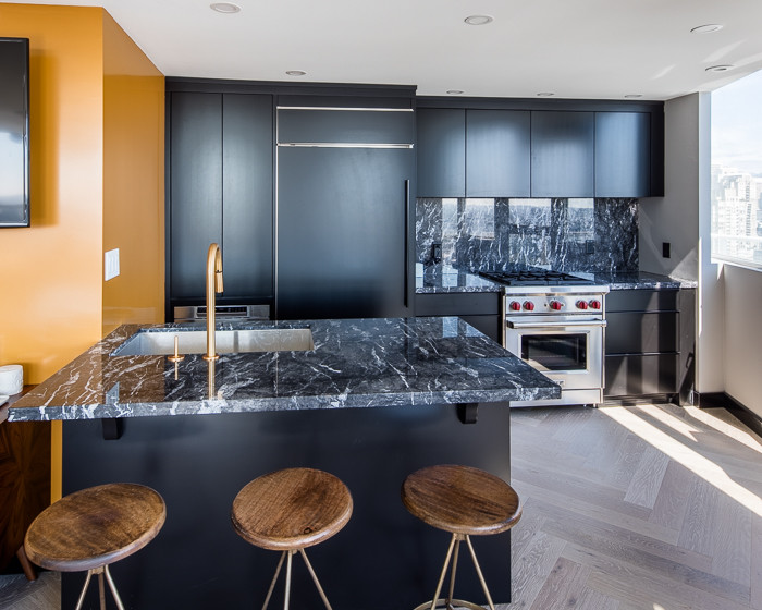 Zweizeilige, Kleine Moderne Wohnküche mit flächenbündigen Schrankfronten, schwarzen Schränken, Marmor-Arbeitsplatte, Küchenrückwand in Schwarz, Rückwand aus Stein, Küchengeräten aus Edelstahl, hellem Holzboden und Kücheninsel in Vancouver