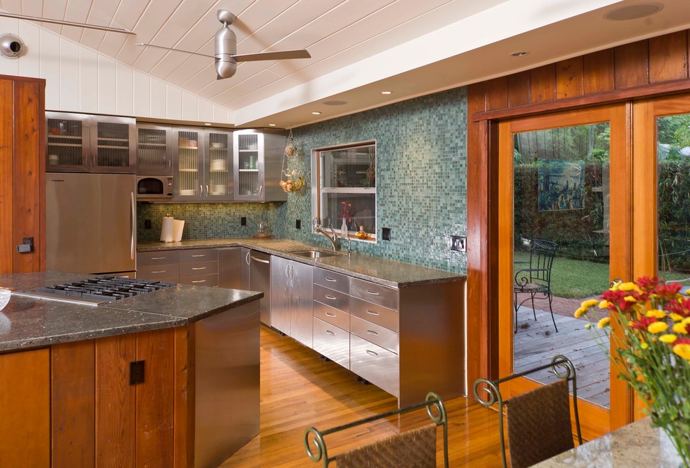 Cette image montre une cuisine américaine design en inox avec un évier encastré, un placard à porte plane, une crédence en mosaïque et un électroménager en acier inoxydable.