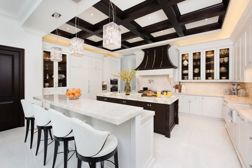 マイアミにある高級なトランジショナルスタイルのおしゃれなキッチン (エプロンフロントシンク、ガラス扉のキャビネット、白いキャビネット、ベージュキッチンパネル、パネルと同色の調理設備、白い床、白いキッチンカウンター、珪岩カウンター) の写真