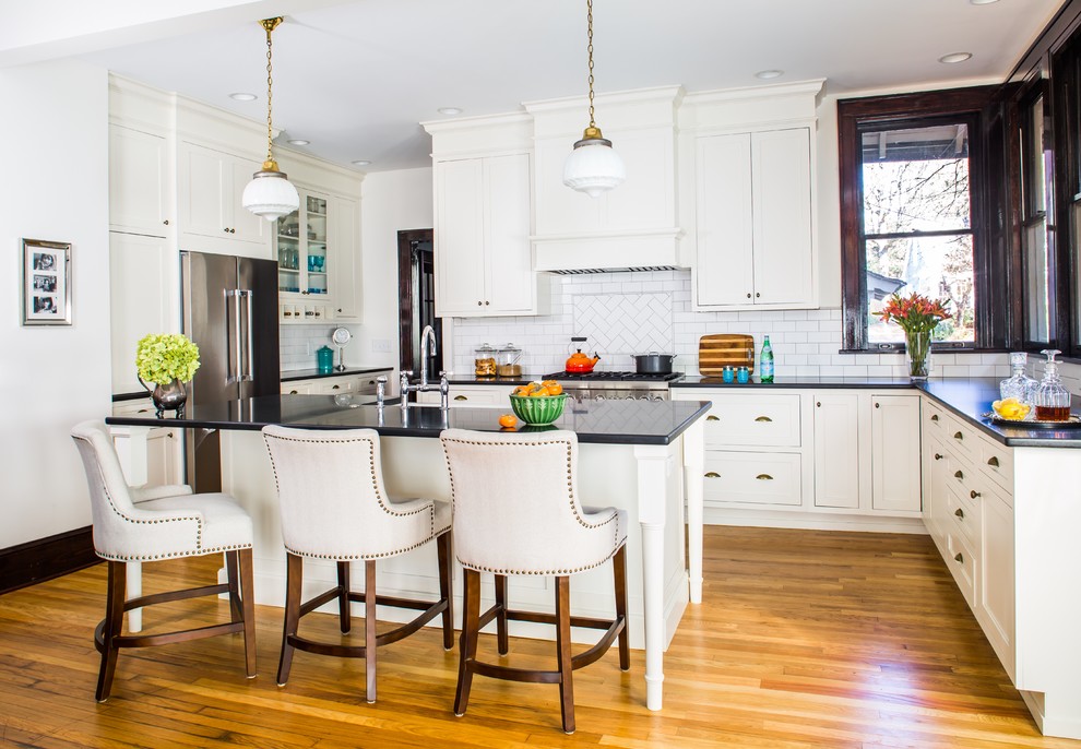 Klassische Küche in L-Form mit Küchenrückwand in Weiß, Küchengeräten aus Edelstahl, Kücheninsel, braunem Holzboden, Schrankfronten im Shaker-Stil, weißen Schränken und Rückwand aus Metrofliesen in Atlanta