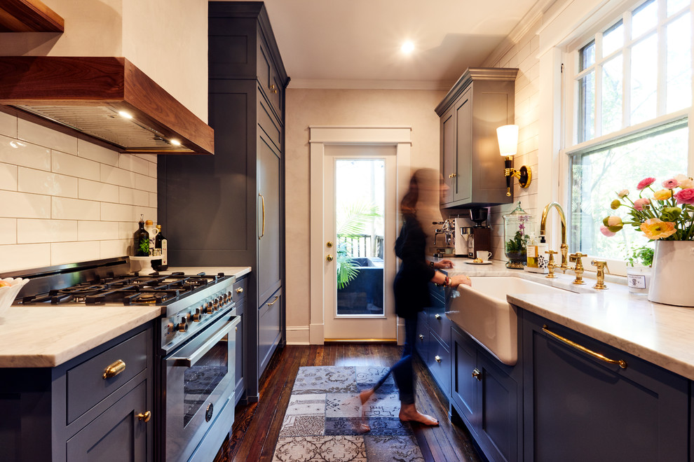 Elegant galley dark wood floor enclosed kitchen photo in Atlanta with a farmhouse sink, shaker cabinets, blue cabinets, white backsplash, subway tile backsplash, stainless steel appliances and no island