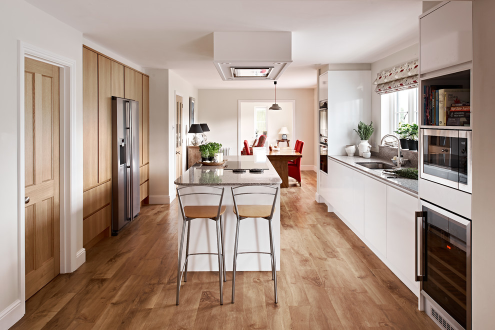Design ideas for a medium sized scandi galley kitchen in Wiltshire with flat-panel cabinets, composite countertops, stone slab splashback, an island, brown floors, a submerged sink, light wood cabinets, stainless steel appliances, light hardwood flooring and grey worktops.