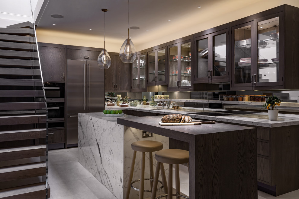 This is an example of a traditional l-shaped kitchen in London with grey floors, a submerged sink, flat-panel cabinets, dark wood cabinets, metallic splashback, mirror splashback, an island and grey worktops.